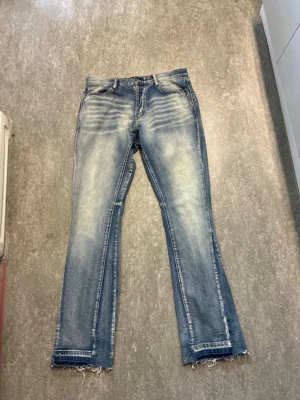 Mnml Blå slitna flared jeans - Ett par ljusblå bootcut jeans med slitningar och fransade benslut. Jeansen har klassisk femficksdesign och tydliga tvättade partier framtill och baktill för en trendig, avslappnad look. Perfekta för dig som gillar en lite mer edgy stil.