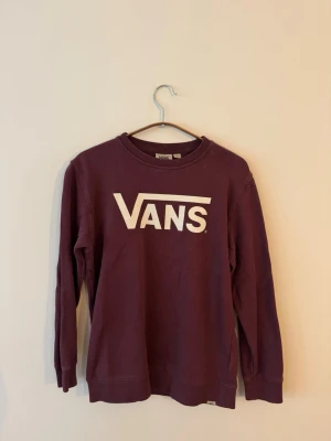 Burgundyröd från Vans - Snygg lila sweatshirt från Vans med stort vitt logotryck på bröstet. Tröjan har rund halsringning, långa ärmar och ribbade muddar vid ärmslut och nederkant. Perfekt för en avslappnad streetstyle-look.