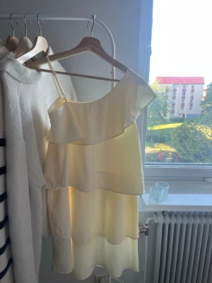 Ljusgul offshoulder volangklänning - Söt ljusgul kortklänning med offshoulder och volangdetaljer. Klänningen har ett axelband och flera lager volanger som ger en romantisk känsla. Perfekt för varma dagar och somriga tillfällen. Någon fläck här och där som inte syns vid användning. Nypris: 499kr