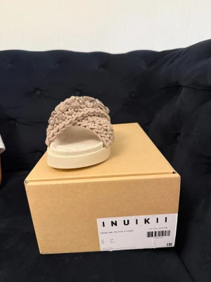 Beige flätade sandaler från Inuikii - Säljer ett par beige sandaler från Inuikii med flätade band och dekorativa stenar. Sandalerna har en chunky, vit sula och breda korslagda remmar i textil. Perfekta för dig som vill ha en unik och trendig look till sommaren. Ordinarie pris 2699kr