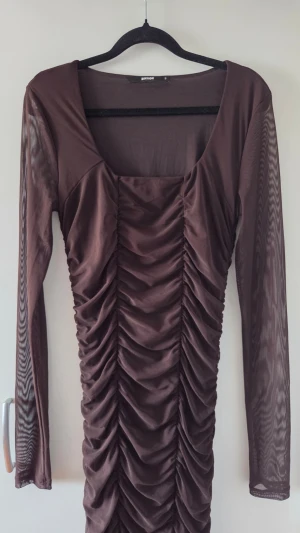 Brun långärmad klänning - Snygg brun klänning med långa ärmar i mesh. Klänningen har rynkade partier nertill som ger en cool och trendig look. Perfekt för party och festliga tillfällen.