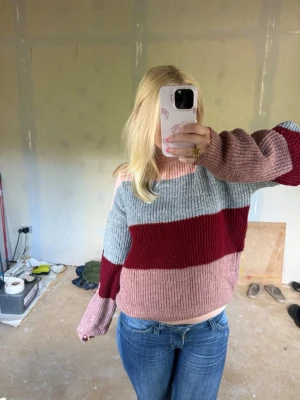 Randig stickad tröja i rosa och vinrött - Mysig stickad tröja med breda ränder i ljusrosa, vinrött och ljusgrått. Tröjan har en avslappnad passform, långa ärmar och ribbstickad struktur. Perfekt för kalla dagar och passar perfekt till jeans. Den saknar en lapp i nacken men är från NA-KD i  storleken M/L🩷 