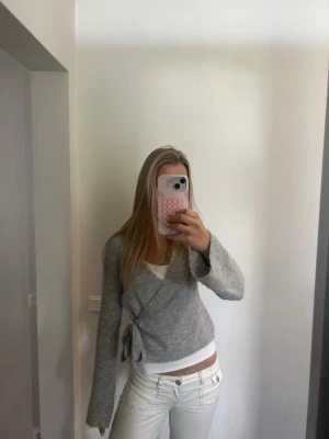 Grå omlottkofta från Gina Tricot - Mysig grå stickad omlottkofta från Gina Tricot i ullblandning. Koftan har långa ärmar, knytband i sidan och en mjuk, fluffig känsla. Perfekt att slänga över en topp för en avslappnad men snygg look.