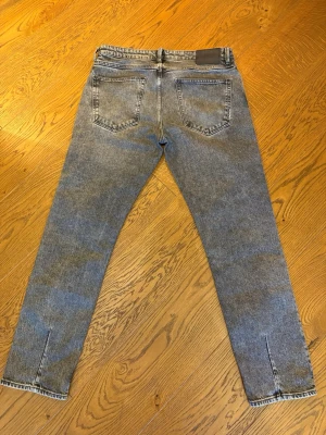 Grå svarta  jeans nuew  - Säljer ett par snygga NEUW jeans i straight fit. Jeansen har en klassisk rak passform och en stilren grå/svart tvätt som passar till det mesta. Modellen är bekväm och fungerar både till vardag och mer uppklädda outfits. Jeansen har deras unika unika detaljer på bakfickan samt öppningen av benen bakifrån   Storlek: 34/32 Skick: Bra skick, sparsamt använda.  Perfekta jeans för dig som vill ha en tidlös och enkel stil.