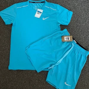 Nike blått träningsset t-shirt & shorts - Snyggt träningsset från Nike i klarblå färg. Setet består av en kortärmad t-shirt och matchande shorts, båda med Nike-logga på bröstet respektive benet. Tillverkade i ett lätt och snabbtorkande material, perfekt för träning eller sportaktiviteter.