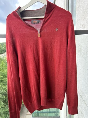 Quarterzip Morris Merinoull Storlek XL Vinröd - Snygg röd stickad tröja från Morris med halv dragkedja och diskret logga på bröstet. Tröjan har ribbade muddar och en klassisk passform. Perfekt för lager på lager och funkar året runt. Materialet känns mjukt eftersom det är merinoull. Plagget är väldigt sparsamt använt 