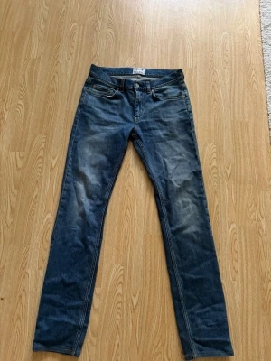 Acne jeans - Säljer ett par blå slim fit jeans med snygga slitningar på låren och knäna. Klassisk femficksmodell med dragkedja och knapp i midjan. Jeansen har en smal passform och är tillverkade i denim med lätt stretch för skön känsla.