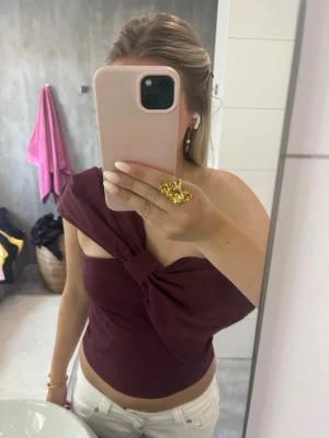 Vinröd oneshoulder topp med rosett - Säljer en vinröd oneshoulder topp med rosett. Storlek M men passar mig som har storlek S.