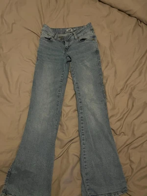 Ljusblå bootcut jeans - Säljer ett par ljusblå bootcut jeans med låg midja. Jeansen har en lätt tvättad look och är tillverkade i denim med lite stretch för skön passform. Perfekta till en avslappnad stil.