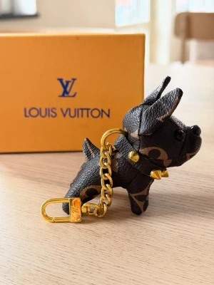  Vuitton hund nyckelring - Säljer en exklusiv Vuitton nyckelring i form av en hund. Tillverkad i brunt monogramläder med guldfärgade metalldetaljer och nitar. Perfekt accessoar för att piffa upp väskan eller nyckelknippan.