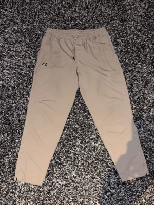 Träningsbyxor från Under Armour - Snygga beige Träningsbyxor från Under Armour. Väldigt bra skick men de är små fläckar på högerbenet men de syns inte om man inte kollar nära. Pris går att diskutera