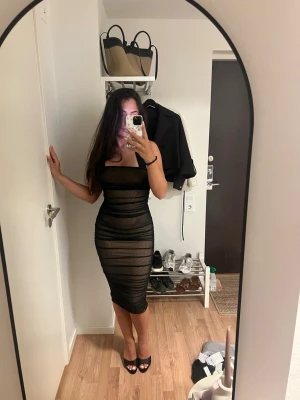 Oh polly klänning  - Säljer en svart, tight meshklänning med ärmlös design med band runt nacken. Klänningen är midilång och har en transparent look med underklänning. Endast använd 1-2 gånger. 