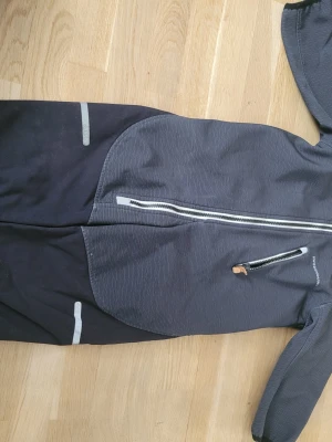 Mörkgrå overall från swedemount - Mörkgrå overall från swedemount med dragkedja framtill och reflexdetaljer på ben och bröst. Overallen har en bröstficka med dragkedja och är tillverkad i ett slitstarkt material, perfekt för utomhusaktiviteter.