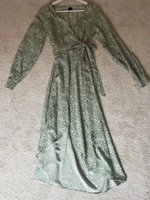 Grön blommig omlottklänning med knyt - Söt långklänning från Vero Moda i ljusgrönt med vitt blommönster. Klänningen har omlottmodell med v-ringning, knyt i midjan och långa ärmar med smock vid ärmsluten. Perfekt för vår och sommar när du vill känna dig extra fin.