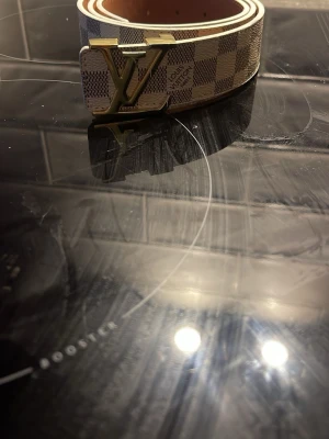 Ett rutformat bälte med ett l-v spänne  - Snyggt bälte med rutformat mönster 