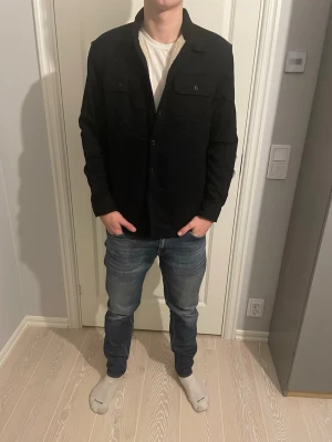 Overshirt Jack and Jones fodrad  - Tja säljer nu en stilren svart fodrad overshirt från Jack and Jones med mjukt beige teddyfoder på insidan. Obershirten har två bröstfickor med stängning, knäppning framtill och klassisk krage. Perfekt lager-på-lager-plagg för en avslappnad och clean outfit perfekt nu till våren med en fodrad fet overshirt🤩storlek M passar mig som är 183 (se bilder)🤗skick 10/10 som ny😁har du någon fråga eller fundering så är de bara att höra av sig🙌🏼mvh premium fashion😁
