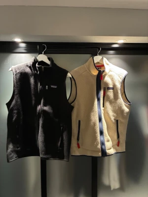 Patagonia fleeceväst svart - 1200 för båda - 700 styck. Svart och beige fleeceväst från Patagonia med hel dragkedja framtill och två sidofickor med dragkedja. Klassisk ståkrage och diskret logga på bröstet. Perfekt för lager-på-lager och outdoor-stil.