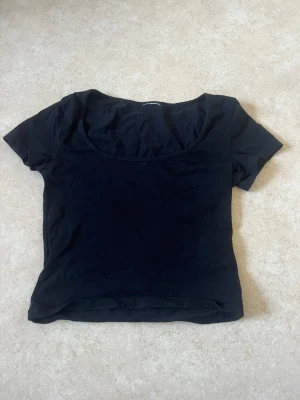 Svart croppad topp med rund hals - Vanlig svart T-shirt med urringning. Den har ett litet hål på framsidan men går att sy lätt eller ha svart topp under 