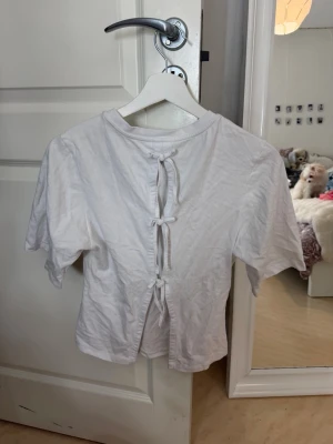 Vit topp med knyt bak - Säljer en vit croppad topp med korta ärmar och rund hals. Toppen har snygga knytband längs ryggen.🤍