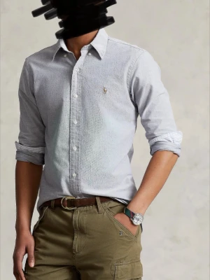 Ljusblå skjorta från Ralph Lauren - Klassisk ljusblå skjorta från Ralph Lauren med button-down krage och broderad logga på bröstet. Skjortan har vita knappar och är tillverkad i mjuk bomull. Perfekt till både jeans och chinos för en clean look.