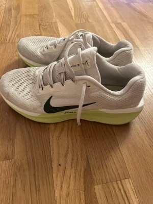 Nike vita sneakers med limegrön sula - Snygga vita Nike sneakers med svart swoosh och limegrön sula. Ovandelen är i mesh för bra ventilation och skon har klassisk låg profil. Perfekta för dig som gillar sportig stil och vill ha bekväma skor till vardags. Skorna har snörning och diskreta detaljer.