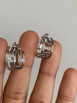 s925 Silvriga örhängen med mönster - Säljer ett par coola silvriga örhängen i hoops-modell med snygga utskurna detaljer och graverat mönster. De har en unik design med geometriska former och passar perfekt för dig som gillar statement-smycken. Materialet är metall i sterling silver coated s925 stamped
