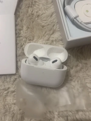 Apple AirPods Pro trådlösa hörlurar - Säljer ett par vita Apple AirPods Pro med laddningsetui. Hörlurarna är in-ear och har en stilren, kompakt design i plast. Perfekta för dig som vill ha trådlös frihet och snygg teknik i vardagen. Laddningskabel och originalförpackning medföljer.