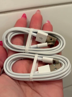 Vita Lightning till USB-laddkablar - Två stycken vita laddkablar med USB-A till Lightning-kontakt, perfekta för att ladda och synka din iPhone eller iPad. Kablarna är smidiga och flexibla med klassisk Apple-design och passar till de flesta Apple-enheter med Lightning-port.