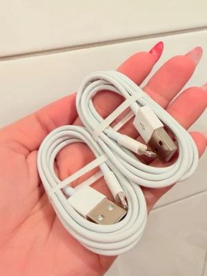 2-pack vita USB till Lightning-kablar - Två stycken vita USB till Lightning-laddkablar, perfekta för att ladda iPhone eller iPad. Kablarna är smidiga och flexibla med klassisk rund form och passar till Apple-enheter med Lightning-port. Perfekt att ha extra hemma eller i väskan.
