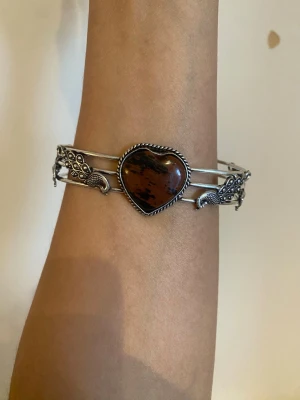 s925 Silverarmband med hjärtformad sten - Unikt armband i äkta silver med en stor hjärtformad brun sten i mitten. Armbandet har detaljerade påfågelsmotiv på sidorna och består av tre tunna silverband. Perfekt för dig som gillar boho eller vintageinspirerad stil. material: sterling silver pläterat s925 stamped