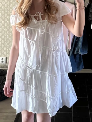 Vit sommarklänning med volanger - Söt vit klänning med volanger och korta ärmar. Klänningen har knytning vid halsen