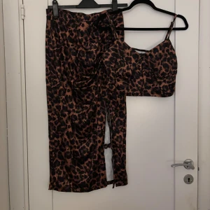 Leopardmönstrat set med topp och kjol - Säljer ett trendigt leopardmönstrat set med en croppad topp med smala axelband och en matchande kjol med slits. Setet har en figurnära passform och är tillverkat i ett stretchigt material som sitter snyggt på kroppen. Perfekt för dig som vill sticka ut.
