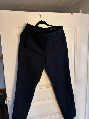 Mörkblå randiga kostymbyxor STOCKH LM - Snygga mörkblå kostymbyxor från STOCKH LM med tunna vita kritstrecksränder. Klassisk rak passform med fickor i sidorna. Perfekta för en stilren look. Materialet känns mjukt och följsamt.