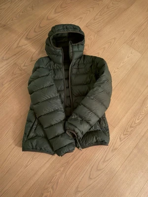 Mörkgrön pufferjacka med huva - Mörkgrön peak performance jacka, funkar på vinter vår och sommar. Storlek S. 