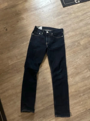 Mörkblå slim jeans från H&M - Snygga mörkblå slim fit jeans från H&M med klassisk femficksdesign och smal passform. Perfekta för dig som gillar en stilren look. Jeansen har orangea sömmar och är tillverkade i bomullsblandning.