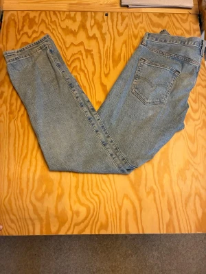 Levi's 501 ljusblå raka jeans - Klassiska Levi's 501 jeans i ljusblå denim med rak passform. Jeansen har fem fickor, knappgylf och den ikoniska läderpatchen bak i midjan. Perfekta för en avslappnad och tidlös stil.