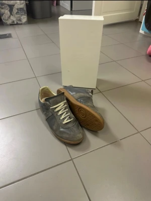 Maison Margiela gats - Maison Margiela sneakers i grå mocka och skinn med beige snörning och gummisula. Klassisk low-top siluett med rund tå och diskret branding på sulan. Tillverkade i Italien, stilrena och passar perfekt till streetwear eller casual outfits sista bilden är tydlig och du som köper ser hur de ser utt.