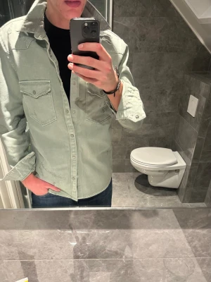 Grön jeansjacka med fickor  - Säljer en stilren ljusgrön jeansjacka med klassisk krage och två bröstfickor med lock. Jackan har raka ärmar och knäppning framtill. Perfekt nu till våren. Jag på bilden är 188cm och bär storlek M. Hör av er vid funderingar :)