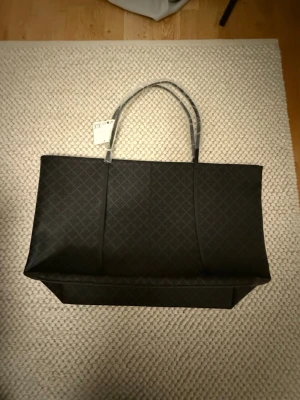 By Marlene birger väska Brun 🤎 - Snygg och rymlig svart shoppingväska med diskret rutmönster. Väskan har långa handtag och dragkedja upptill. Insidan är beige och har en innerficka. Perfekt för dig som vill ha plats för allt du behöver under dagen.