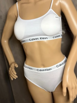Vitt underklädesset från Calvin Klein M-Lsize - Säljer ett vitt underklädesset från Calvin Klein med sportig topp och matchande trosor. Båda delarna har elastiska band med logotypen tryckt i svart. Materialet är mjukt och stretchigt, perfekt för en bekväm känsla hela dagen.