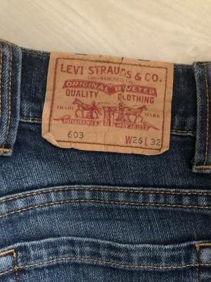 Levi's blå raka jeans W25 L32 - Klassiska blå jeans från Levi's med raka ben och femficksmodell. Jeansen har tydliga kontrastsömmar och är tillverkade i slitstark denim. Perfekta för en avslappnad och tidlös look.