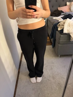 Svarta mjukisbyxor från Gina  - Ett par klassiska svarta mjukisbyxor med resår i midjan och dragsko för skön passform. Byxorna har raka ben och är tillverkade i mjukt, bekvämt material som passar perfekt för chill dagar hemma eller när du vill vara extra bekväm.