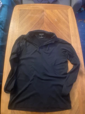 Svart långärmad tröja Emporio Armani - Stilren svart långärmad tröja från Emporio Armani med hög krage och dragkedja vid halsen. Tillverkad i mjukt material som känns bekvämt mot huden. Perfekt för dig som gillar en enkel men exklusiv look.