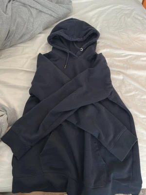 Svart oversized hoodie med huva - En svart oversized hoodie med stor huva och dragsnören. Hoodien har en klassisk känguruficka framtill och ribbade muddar vid ärmslut och nederkant. Perfekt för en chill och avslappnad stil. Materialet känns mjukt och bekvämt, troligen bomullsblandning.