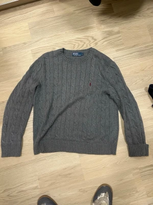 Grå stickad Ralph Lauren tröja  - Stickad grå tröja från Ralph Lauren. Klassisk design med röd broderad logga på bröstet. 