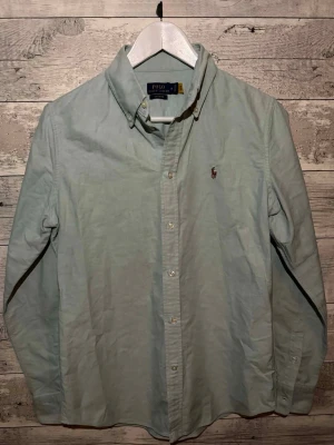 Ljusblå skjorta från Polo Ralph Lauren - Klassisk ljusblå skjorta från Polo Ralph Lauren med button-down krage och broderad logga på bröstet. Skjortan har långa ärmar, knappar framtill och är tillverkad i mjuk bomull. Perfekt för en clean och stilren look.