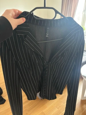 Svart randig skjorta från Amisu - Snygg svart skjorta från Amisu med vita tunna ränder. Skjortan har klassisk krage, knäppning framtill och långa ärmar. Perfekt för en stilren look och passar till många olika outfits.