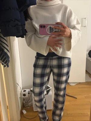 Rutiga pyjamasbyxor i blått och vitt - Säljer ett par mysiga pyjamasbyxor med blått och vitt rutmönster. Byxorna har en klassisk rak passform och resår i midjan för extra komfort. Perfekta för slappa dagar hemma eller när du vill chilla i soffan.