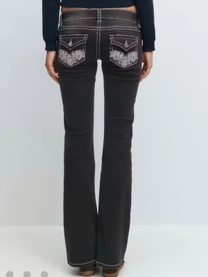 Svarta bootcut jeans med brodyr - Snygga svarta bootcut jeans med vit kontrastsöm och broderade bakfickor. Jeansen har låg midja och utsvängda ben, vilket ger en retrovibe. Materialet är klassisk denim med stretch för extra komfort.