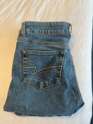 Blå bootcut jeans med broderad ficka - Blåa bootcut jeans med broderi på bakfickan.                                                                 Lågmidjade                                                             Storlek S och normal stora 